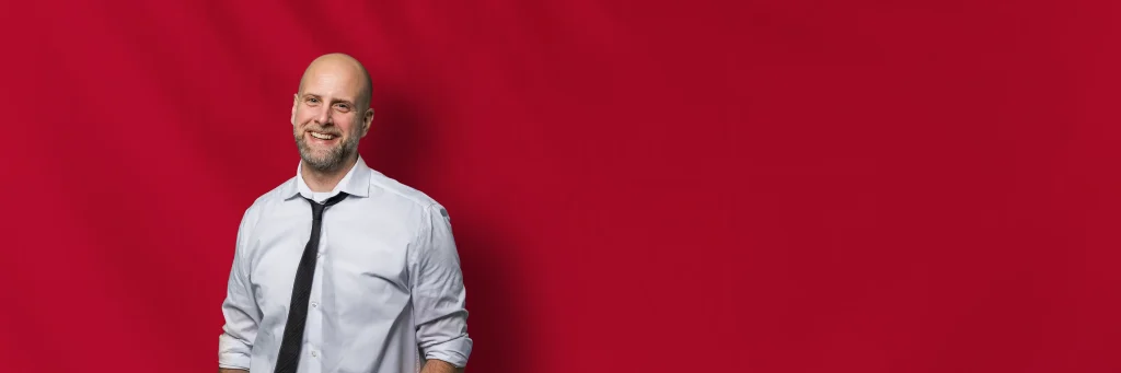 DJ Markus Bogi vor rotem Hintergrund lächelnd