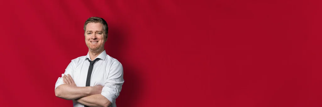 DJ Christian vor rotem Hintergrund mit verschränkten Armen